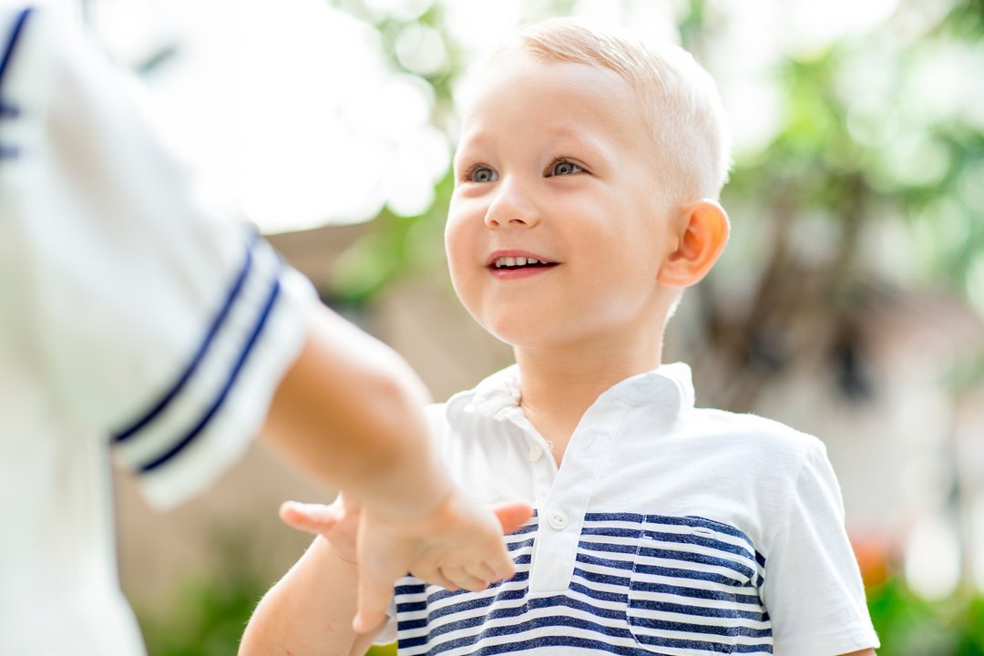 Ein 4-jähriger Junge lächelt mit leuchtenden Augen sein Gegenüber an und nutzt unterstützend seine Hände