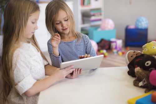 Zwei Mädchen im Kinderzimmer schauen auf ein Tablet und unterhalten sich über die Inhalte