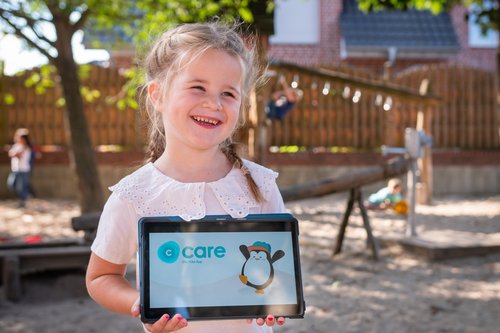 Ein Kita-Kind zeigt lachend das Tablet mit der CARE Kita-App
