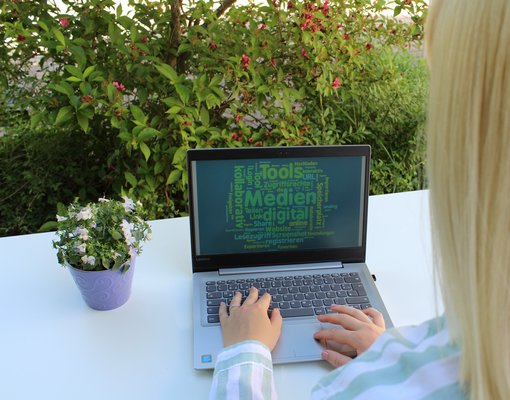 Eine Frau arbeitet im Freien am Laptop und bildet eine Schlagwortwolke