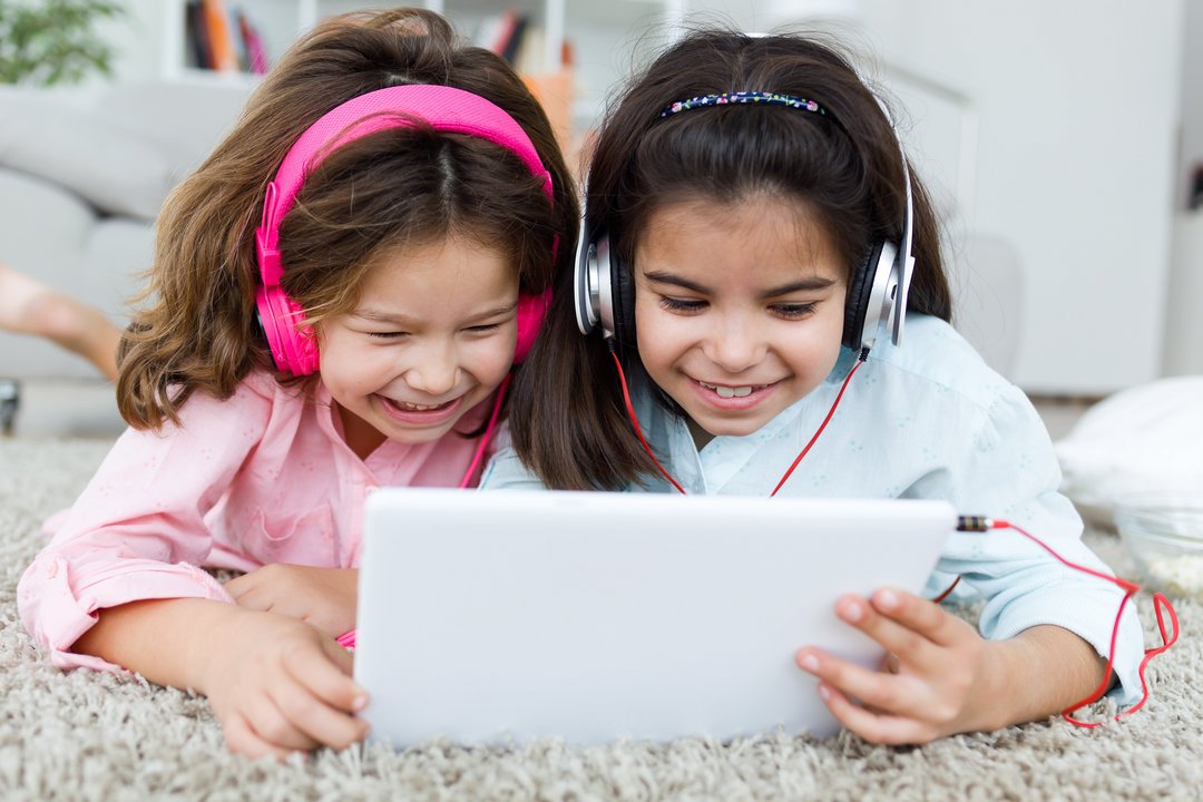Zwei Mädchen mit Kopfhörern schauen gemeinsam ins Tablet und lachen