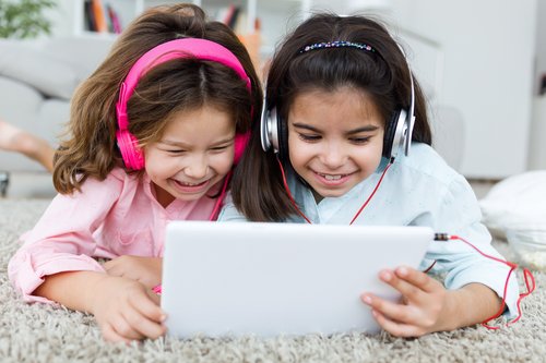 Zwei Mädchen mit Kopfhörern schauen gemeinsam ins Tablet und lachen